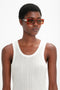 Person wearing a white sleeveless top and large, rectangular Chain Detail Rectangular Frame Sunglasses In Striped Blonde Havana by Victoria Beckham stands against a plain white background.