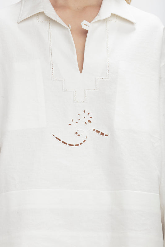 Close-up of a vintage-inspired white garment featuring a V-shaped neckline and embroidered cutout design with geometric shapes and floral elements: the Victoria Beckham Oversized Embroidered Tunic In Antique White.