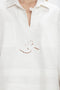 Close-up of a vintage-inspired white garment featuring a V-shaped neckline and embroidered cutout design with geometric shapes and floral elements: the Victoria Beckham Oversized Embroidered Tunic In Antique White.