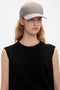 Young woman wearing a black sleeveless top and a gray wool Victoria Beckham Logo Cap In Dogtooth Check, posing against a white background.