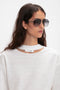 A person with long, dark hair wearing Victoria Beckham's V Metal Pilot Sunglasses In Grey Gradient and a white shirt with a cut-out neckline.