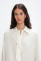 A person with long, dark hair is wearing an Asymmetric Ruffle Blouse In Ivory by Victoria Beckham and is looking directly at the camera against a plain, white background.