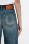 Close-up of a person wearing vintage denim Victoria Beckham Alina High Waisted Jean In Indigrey Wash with a brown leather patch visible on the back waistband, and a white shirt partially tucked in. The person's right arm is hanging by their side.