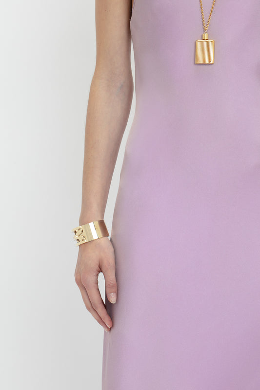 A person wearing a sleeveless, "Low Back Cami Floor-Length Dress In Rosa" by Victoria Beckham with a gold bracelet and a gold pendant necklace, reminiscent of Victoria Beckham's iconic style.