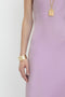 A person wearing a sleeveless, "Low Back Cami Floor-Length Dress In Rosa" by Victoria Beckham with a gold bracelet and a gold pendant necklace, reminiscent of Victoria Beckham's iconic style.