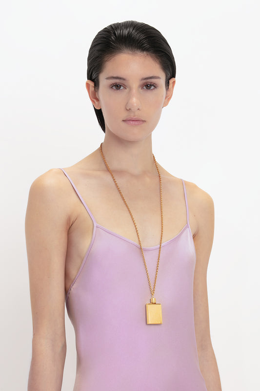 Sure, here's the sentence with the given product name and brand name: 

A person with short hair is wearing a Low Back Cami Floor-Length Dress In Rosa by Victoria Beckham and a long gold chain necklace with a rectangular pendant, reminiscent of Victoria Beckham's elegant style. The background is white.