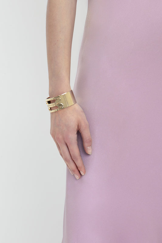 A close-up of a person's left hand adorned with a gold bracelet, resting elegantly against a light purple, satin-like Victoria Beckham Low Back Cami Floor-Length Dress In Rosa.