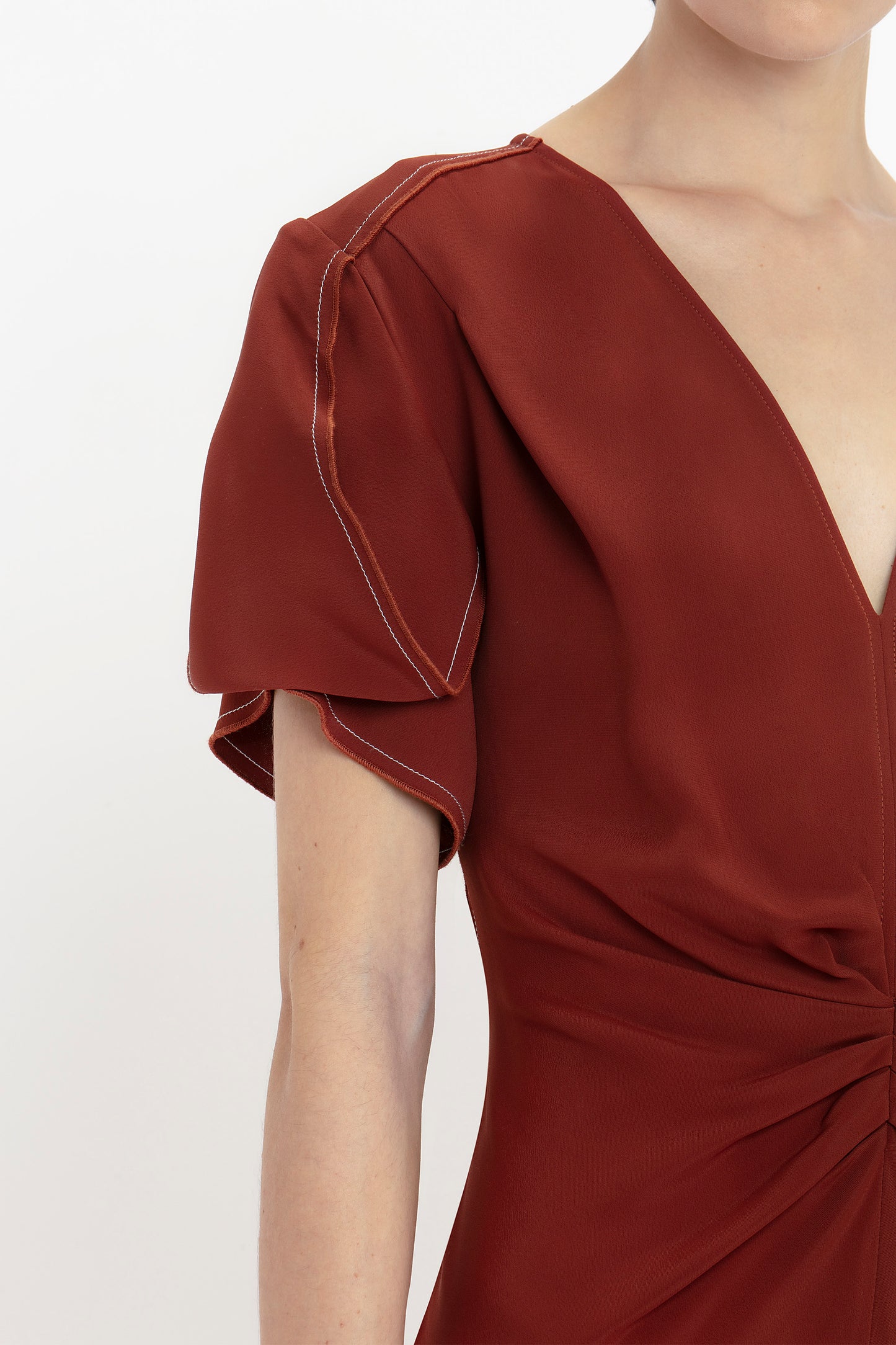 Person wearing a Victoria Beckham Gathered V-Neck Midi Dress In Russet with short, puff sleeves and detailed stitching. The figure-flattering stretch fabric enhances the upper torso focus of the image.