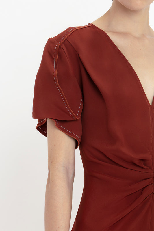 Person wearing a Victoria Beckham Gathered V-Neck Midi Dress In Russet with short, puff sleeves and detailed stitching. The figure-flattering stretch fabric enhances the upper torso focus of the image.