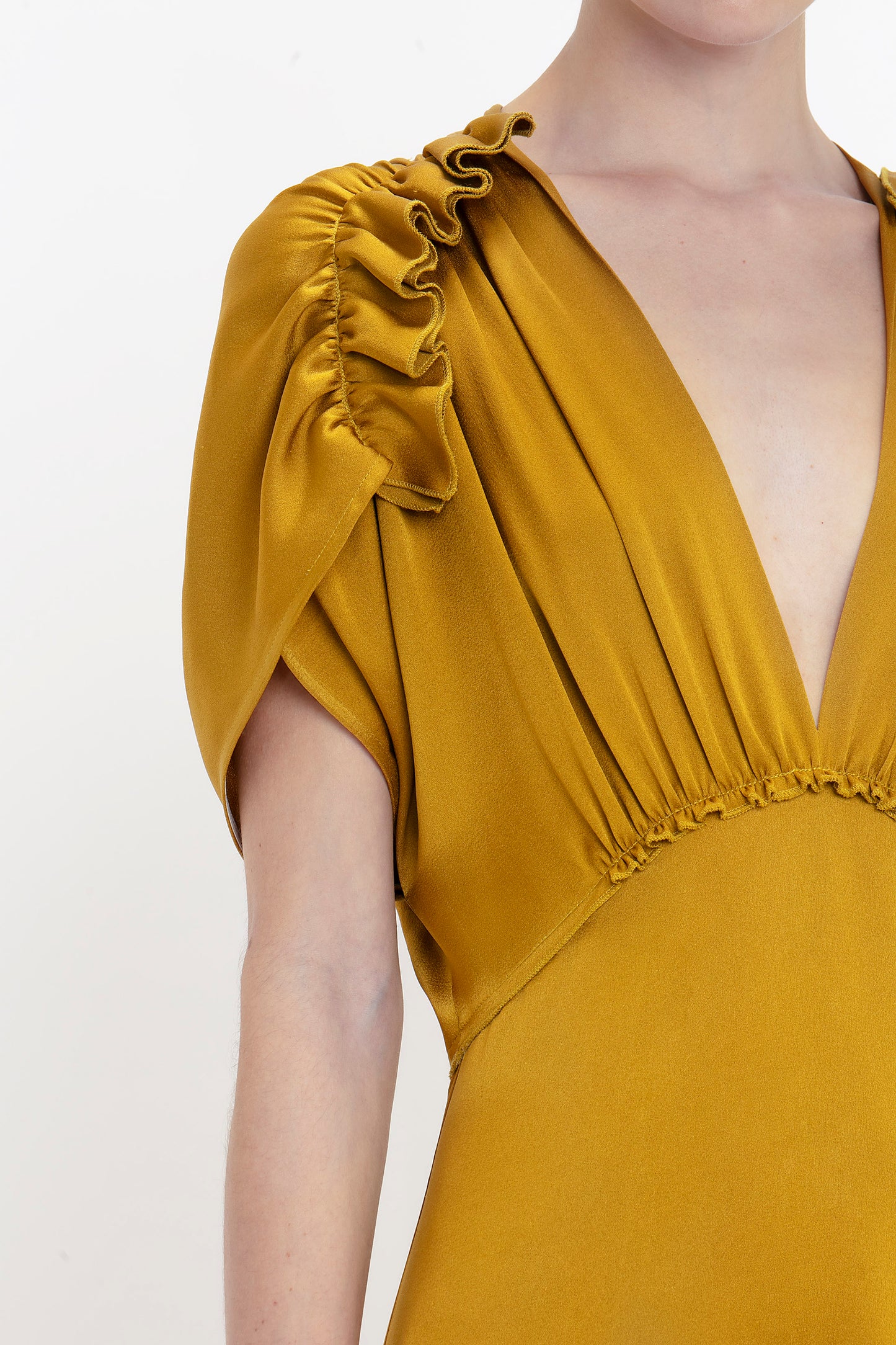 Close-up of a person wearing a Harvest Gold dress with a deep V-neckline and ruched sleeves. This Victoria Beckham V-Neck Ruffle Midi Dress In Harvest Gold has gathered fabric detailing along the waist and shoulders, adding a seductive quality to the overall look.