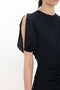 Close-up of a person wearing the Victoria Beckham Gathered Waist Midi Dress In Midnight with open shoulder detail and draped fabric. The classic fit-and-flare design accentuates the gathered waist. The person's head is not visible in the image.