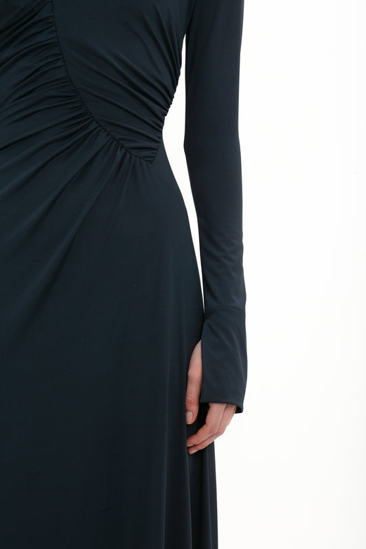 Close-up of a person wearing a black Victoria Beckham Ruched Detail Floor-Length Gown In Midnight with long sleeves and gathered fabric on the side. The individual is partially visible from shoulder to hand, reminiscent of understated elegance that Victoria Beckham is known for in her evening gowns.