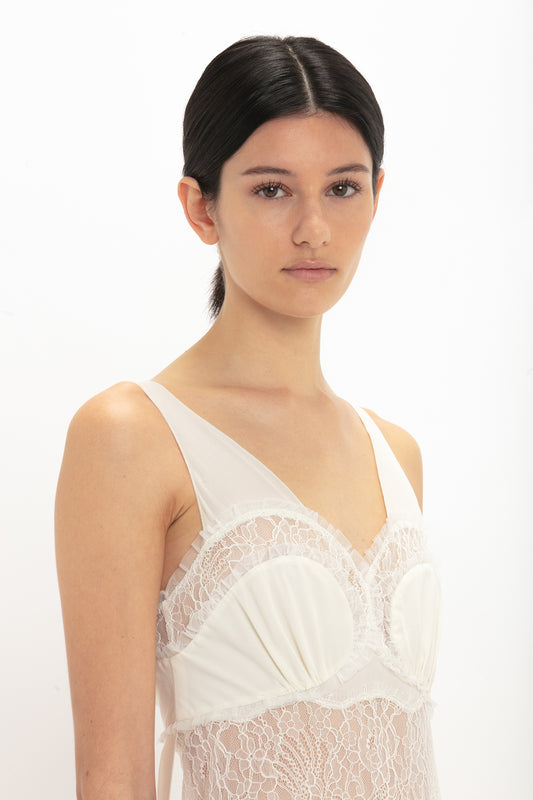 A woman with dark hair tied back is wearing the Victoria Beckham Ruffle Detail Midi Dress In Ivory and looking directly into the camera against a plain white background.