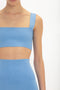 A person is wearing a blue, ribbed, two-piece outfit consisting of a Strap Bandeau Top In Marina by Victoria Beckham and a high-waisted skirt. Their face and lower body are not visible in the image.