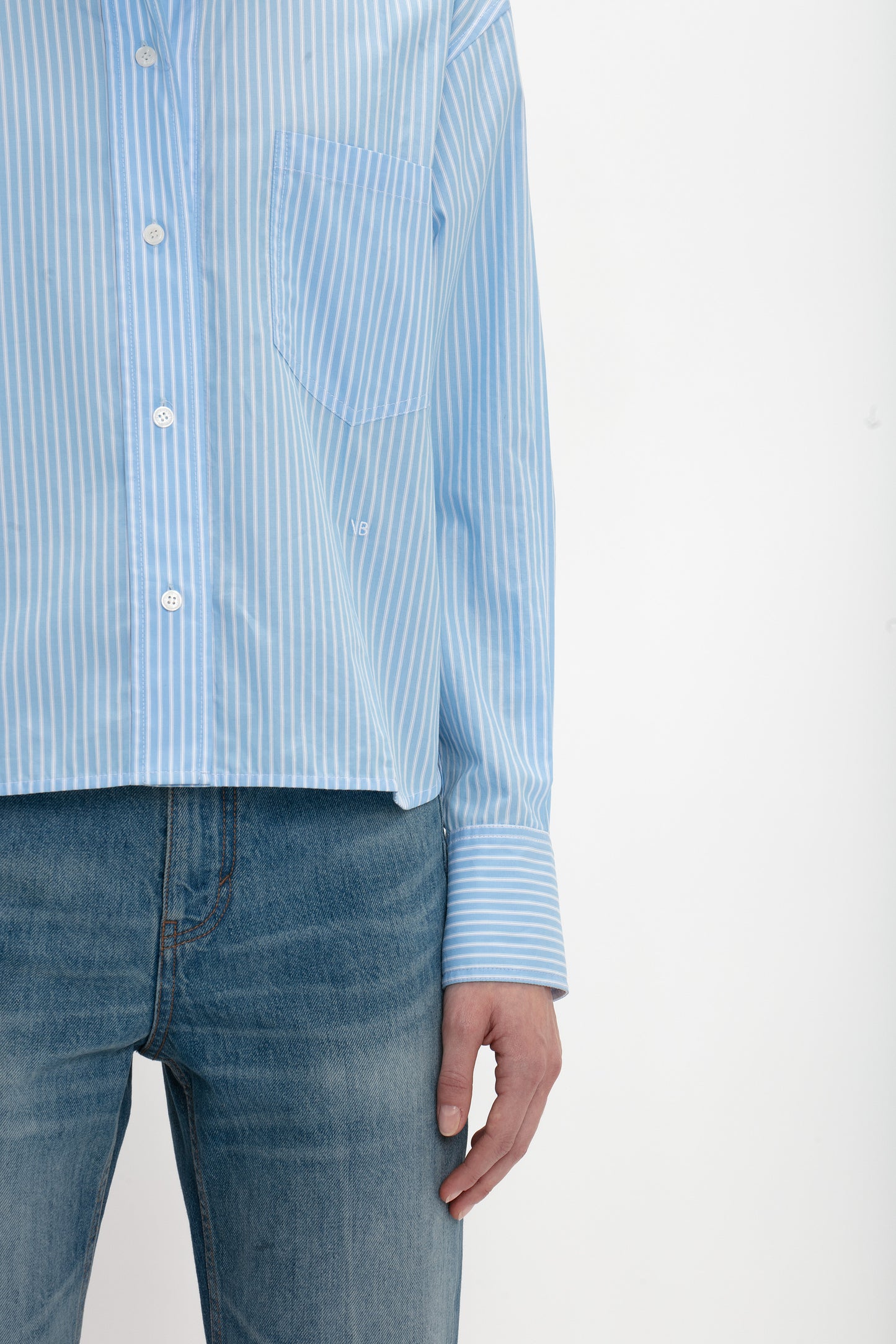 A person wearing a Victoria Beckham Cropped Long Sleeve Shirt In Marina-White and blue jeans stands against a plain white background. Only the torso and part of one arm are visible.