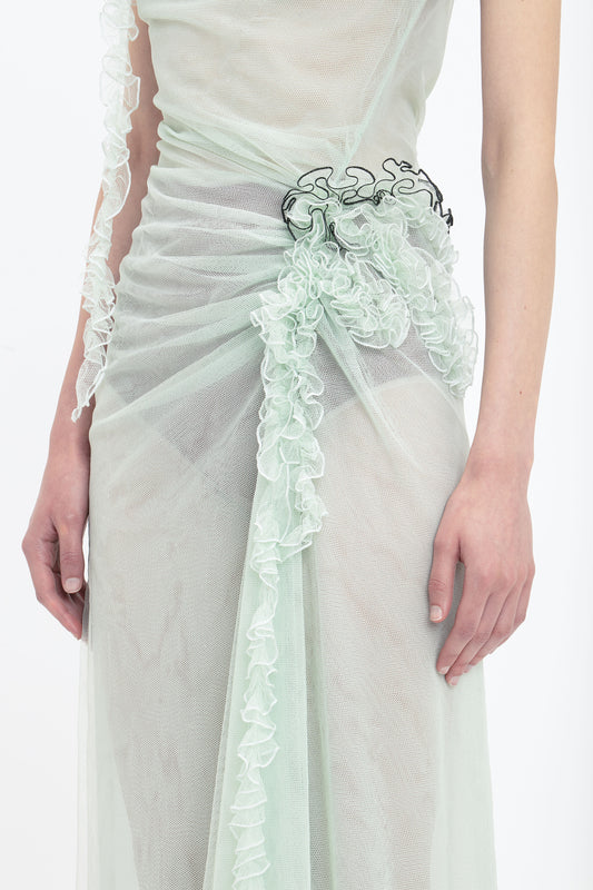 A person is wearing a Gathered Tulle Detail Floor-Length Dress In Jade by Victoria Beckham. The limited edition gown features intricate detailing and gathers at the waist. The person's right arm is visible, and the background is plain white.