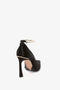 A single Pointy Toe Pump in Black Satin by Victoria Beckham with a closed toe and an ankle strap featuring gold accents and a chic metal ankle bracelet is shown against a white background.