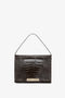 A dark brown, croc-effect Jumbo Chain Pouch Bag In Chocolate Croc-Effect Leather from Victoria Beckham with a gold clasp and a single top handle against a white background, perfect for versatile styling.