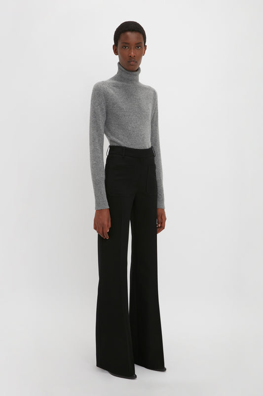 Person standing against a plain background wearing a **Victoria Beckham Polo Neck Jumper In Grey Melange** and black high-waisted, wide-leg pants.