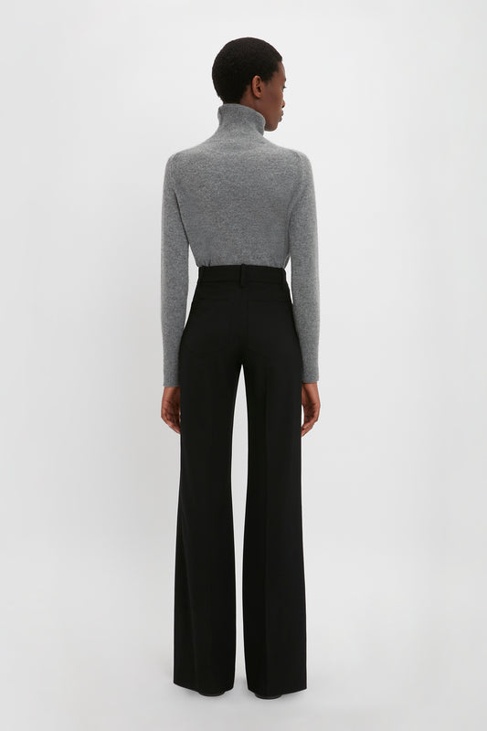Person standing with their back to the camera, wearing a Victoria Beckham Polo Neck Jumper In Grey Melange and black high-waisted, wide-leg pants, showcasing versatile styling options.