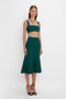 A woman in a flattering flared silhouette poses in a fitted, sleeveless, green VB Body Flared Skirt In Lurex Green by Victoria Beckham against a plain white background.