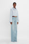 Person wearing a blue and white striped shirt and high-waisted Bianca Jean In Light Blue Denim by Victoria Beckham with center seam detail, stands against a plain white background.