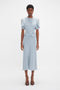 A black woman in a light blue Exclusive Gathered Waist Midi Dress In Pebble by Victoria Beckham, with cold-shoulder sleeves and standing against a white background.