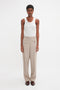 A person with short hair is wearing a Victoria Beckham Fine Knit Vertical Stripe Tank In White and beige pants. They are standing against a plain white background.