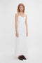 A person stands against a plain white background, wearing a sleeveless, ankle-length Cami Fit And Flare Midi In White by Victoria Beckham made of breathable stretch cotton and dark brown shoes.