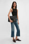 A person with long hair wearing a Victoria Beckham Lightweight Tank Top In Black, cropped blue jeans, and brown shoes is holding a large black Givenchy clutch against a white background.