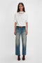 A person stands against a plain white background, wearing a relaxed cut Victoria Beckham Bonded Jersey Tee In White, blue jeans with light wash details, a black belt, and brown ankle boots.