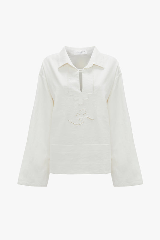 A Victoria Beckham Oversized Embroidered Tunic In Antique White featuring a collar, a V-shaped neckline, and subtle embroidery details on the chest. Made from a linen-cotton blend for added comfort.