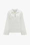 A Victoria Beckham Oversized Embroidered Tunic In Antique White featuring a collar, a V-shaped neckline, and subtle embroidery details on the chest. Made from a linen-cotton blend for added comfort.