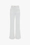 A pair of white high-waisted, wide-flared leg jeans with front pockets and a front button and zipper closure, offering a retro appeal, now available as the Alina High Waisted Jean In Washed White by Victoria Beckham.