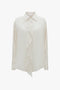 An Asymmetric Ruffle Blouse In Ivory by Victoria Beckham with a collared neckline and voluminous sleeves is displayed against a plain background.