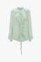 A Romantic Blouse In Jade by Victoria Beckham with diaphanous blouson sleeves, a ruffled front, high neckline, and tie detail.