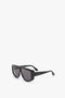 Black rectangular sunglasses with black tonal lenses and a slim frame. The arm of the Acetate Visor Sunglasses In Black by Victoria Beckham has a small gold-colored inscription.