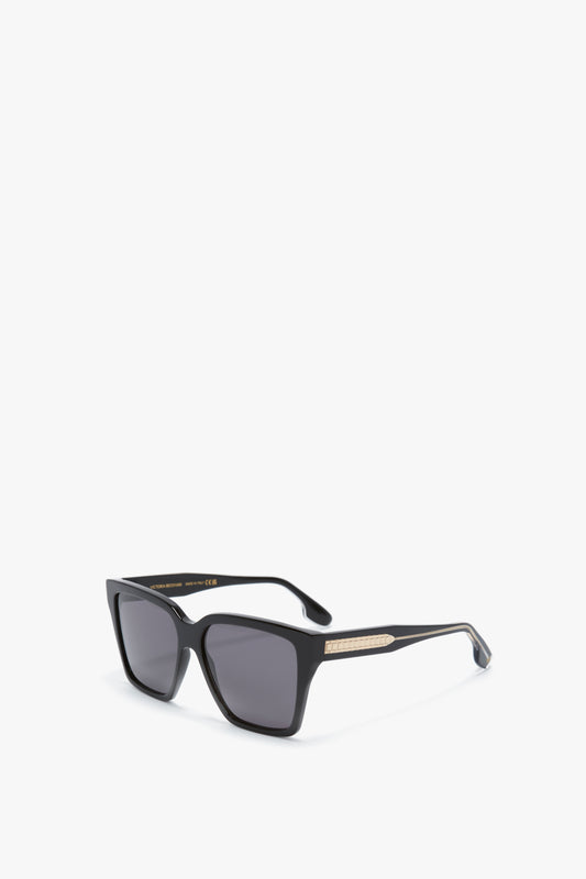 Victoria Beckham Soft Square Frame Sunglasses In Black features dark lenses and gold accents on the arms, displayed on a white background.