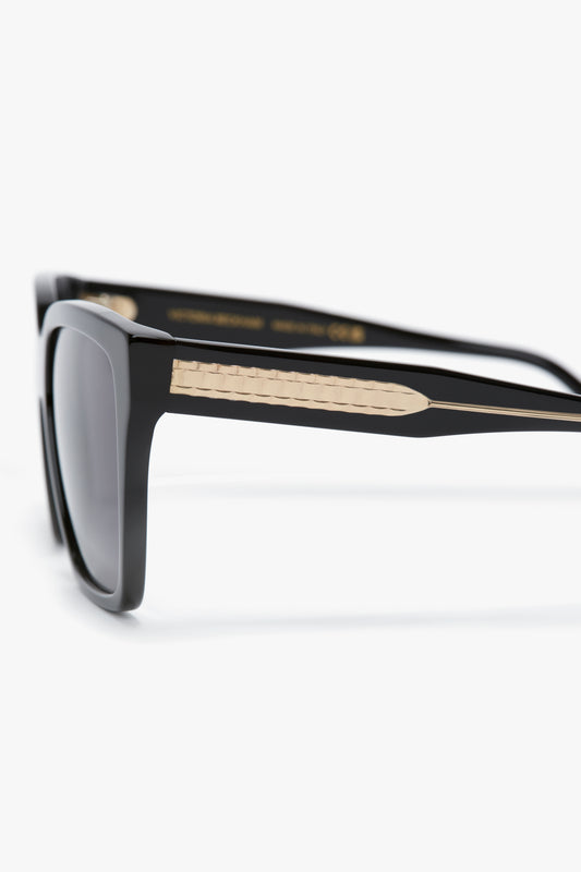 Close-up of Soft Square Frame Sunglasses In Black with a gold accent on the arms. The soft square frame design is sleek and modern, featuring dark tinted lenses, reminiscent of Victoria Beckham eyewear.