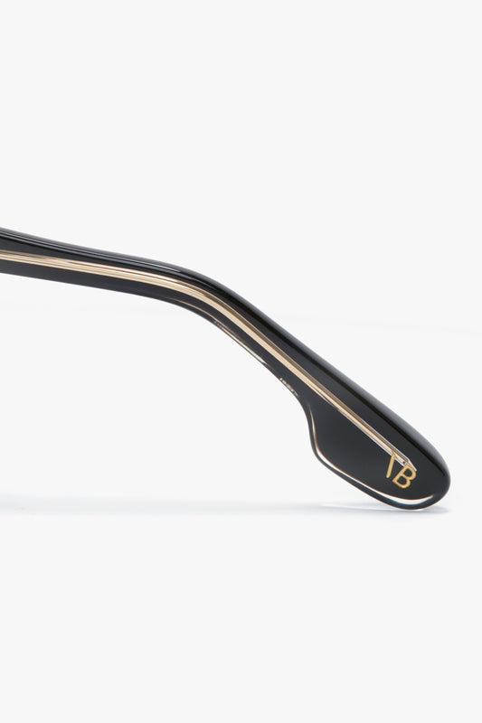 Close-up of a black glasses arm with gold trim and the initials "TB" near the end against a white background, showcasing the elegance of Victoria Beckham Soft Square Frame Sunglasses In Black.