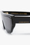 Close-up of a pair of black Layered Lens Visor Sunglasses In Black with thick frames. The temple arm features the text "VICTORIA BECKHAM" in gold lettering, epitomizing the elegance of Victoria Beckham eyewear. This SS24 collection piece boasts a sleek design perfect for any fashion-forward individual.