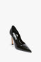 A single, black high-heeled shoe with a pointed toe and a light-colored sole, featuring a sculptural heel and signature V motif, viewed from a slight side angle is the V Pump In Black Brushed Leather by Victoria Beckham.