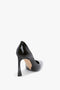 Back view of a black high-heeled shoe with a pointed toe, featuring a sculptural heel and a sleek, smooth finish on a white background. This is the V Pump In Black Brushed Leather by Victoria Beckham.