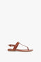 A single brown flat sandal with a thong-style strap, an adjustable ankle strap, and a simple, minimalist design featuring a subtle gold-tone chain detail by Victoria Beckham is the Flat Chain Sandal in Tan Leather.