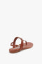 A Victoria Beckham Flat Chain Sandal In Tan Leather, viewed from behind on a white background.