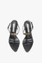 A pair of black, open-toe high-heel sandals with thin ankle straps and gold buckle details, featuring a V-shaped sculptural heel and crafted from supple nappa leather, viewed from above—Frame Detail Sandal In Black Leather by Victoria Beckham.