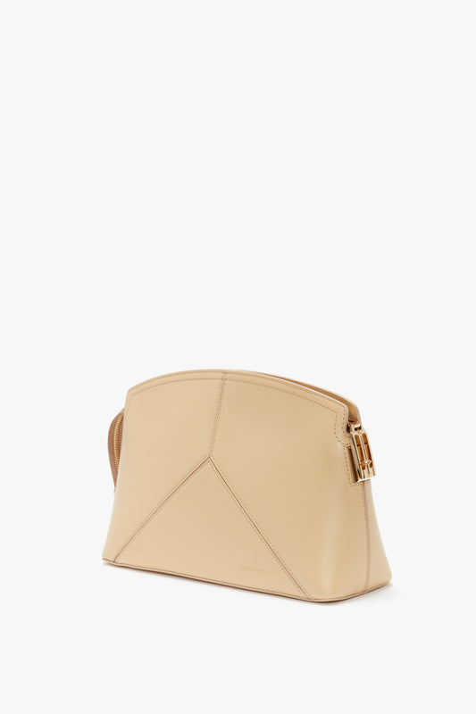 A beige, trapezoidal-shaped Victoria Clutch Bag In Sesame Leather from Victoria Beckham with a geometric design, featuring a gold buckle on the strap and a minimalist style.