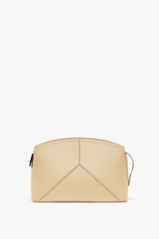 A beige, trapezoidal-shaped calf leather clutch with minimal stitching details and a slim wrist strap on one side, showcased on a white background. This stylish piece epitomizes the elegance seen in Victoria Beckham collections and is perfect for any SS24 runway look. Introducing the Victoria Clutch Bag In Sesame Leather.