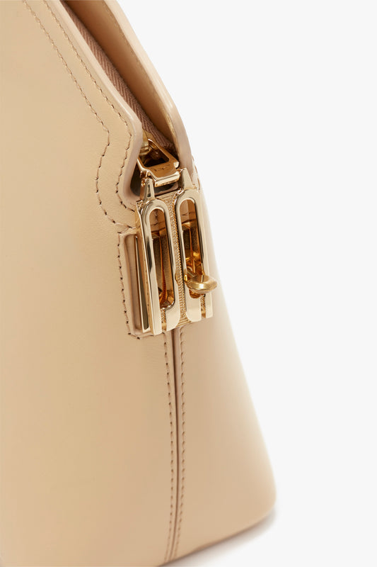 Close-up of a beige calf leather Victoria Clutch Bag In Sesame Leather from Victoria Beckham's SS24 runway, showing a gold clasp detail. The stitching is visible along the edge, highlighting the craftsmanship.