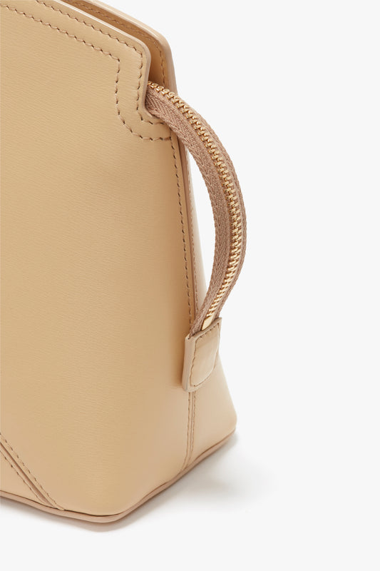 Close-up of a Victoria Clutch Bag In Sesame Leather from Victoria Beckham with a curved handle attached to its side. The stitching and texture of the leather are visible, reminiscent of designs seen on the SS24 runway.